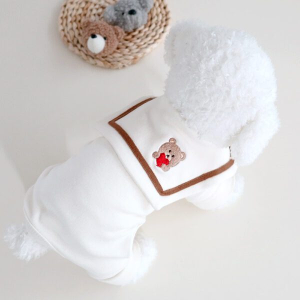 A white dog wearing a brown vest next to a basket of teddy bears.